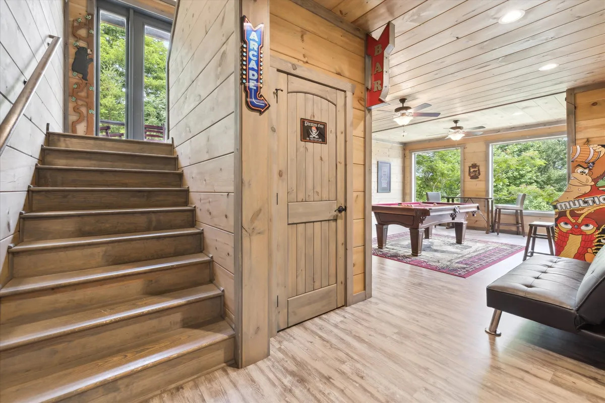 A vibrant interior game room with a pool table, wooden bar area, staircase, and large windows letting in natural light and offering a glimpse of the outdoors. The space is designed for fun and socializing, echoing the atmosphere of friendly competition and entertainment described in the section.