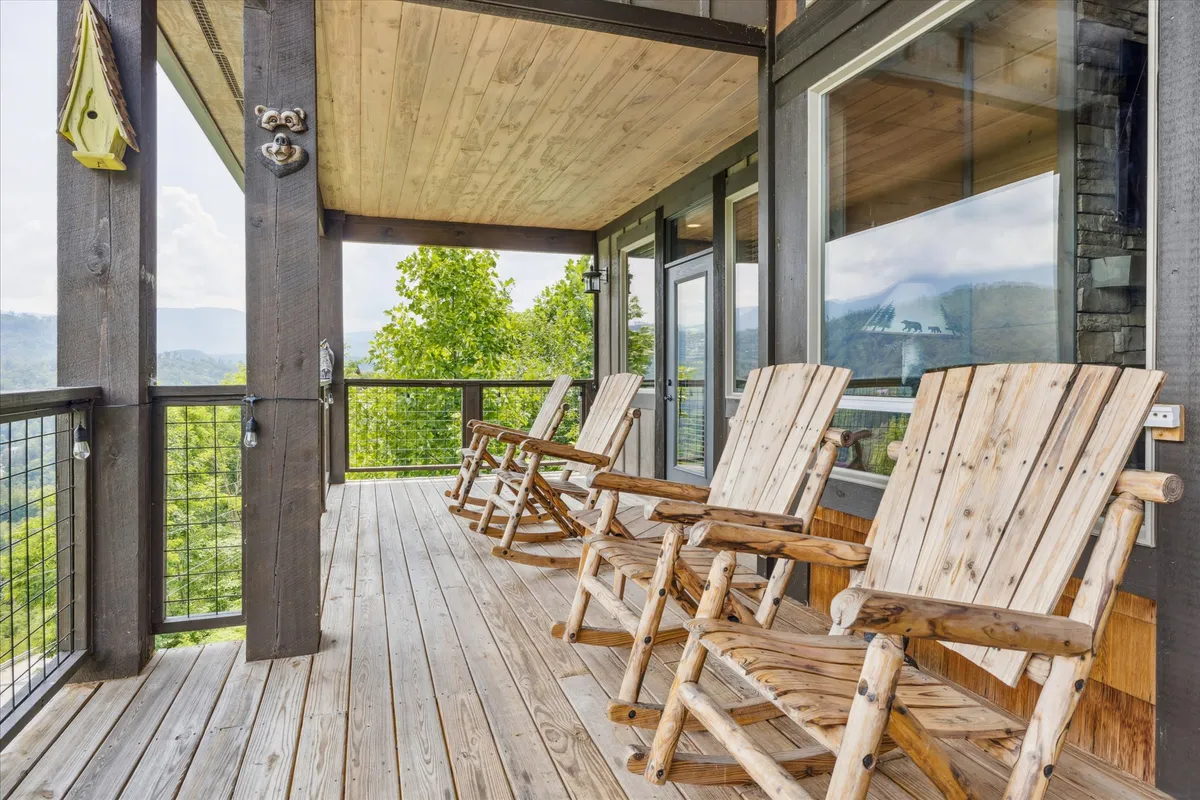 A spacious wooden deck with classic rocking chairs and a scenic view of the surrounding mountains and forest. The setting is designed for relaxation, socializing, and taking in the sights and sounds of nature, emphasizing a seamless connection to the outdoors.