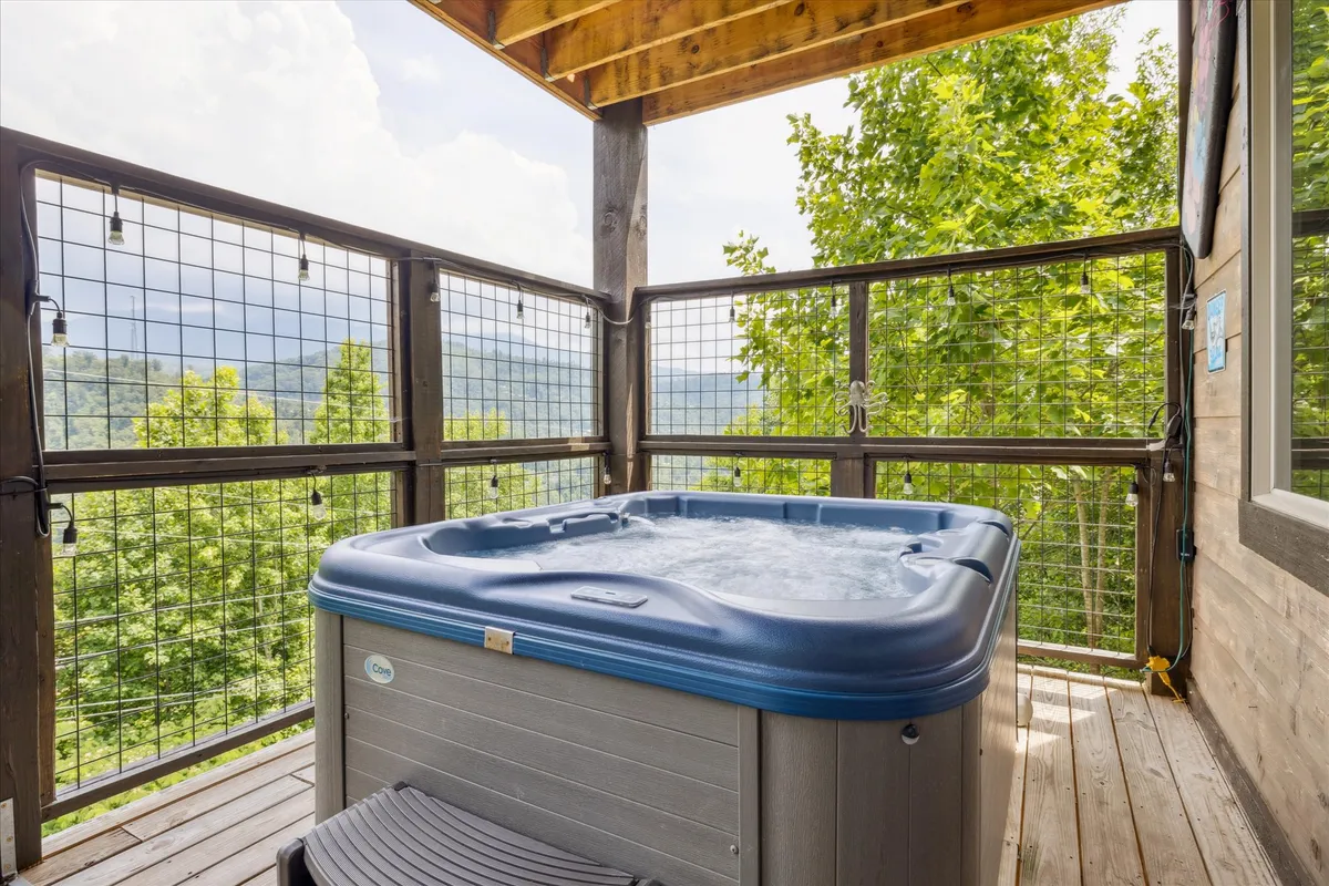 This image shows a serene outdoor scene featuring a hot tub on a wooden deck, overlooking a stunning mountain view. The setting sun bathes the mountainside in golden light, while the deck invites relaxation after a day of adventure.